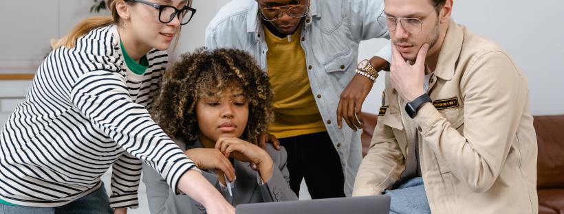 Four people stand around a laptop talking to each other.